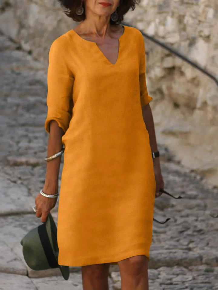 Front view of a woman wearing an orange vintage solid mini dress with a V-neck and three-quarter sleeves