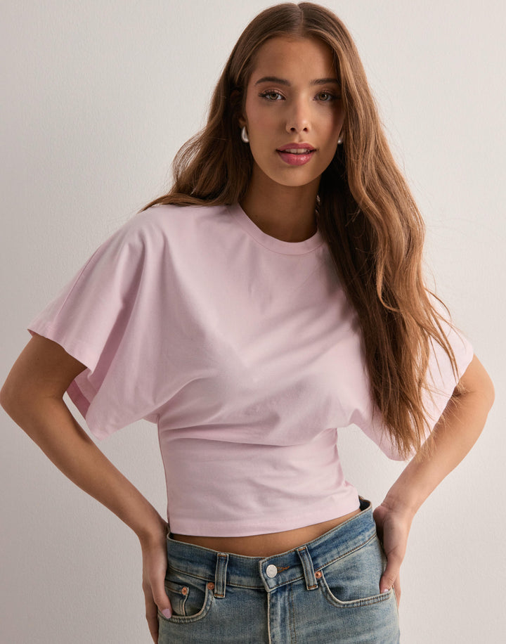 Front view of a model wearing a pink oversized icon tee with wide sleeves and light wash jeans