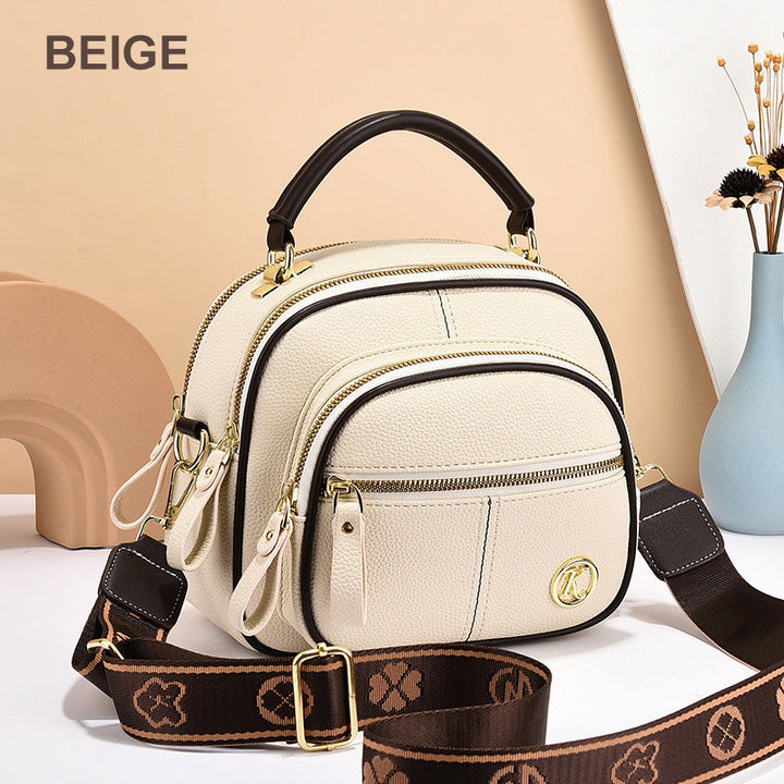 Front view of a beige leather crossbody bag with a dark top handle and a patterned shoulder strap