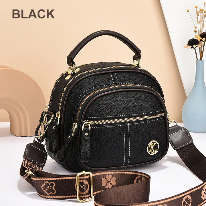 Front view of a black leather crossbody bag with white stitching, gold zips, and a patterned shoulder strap