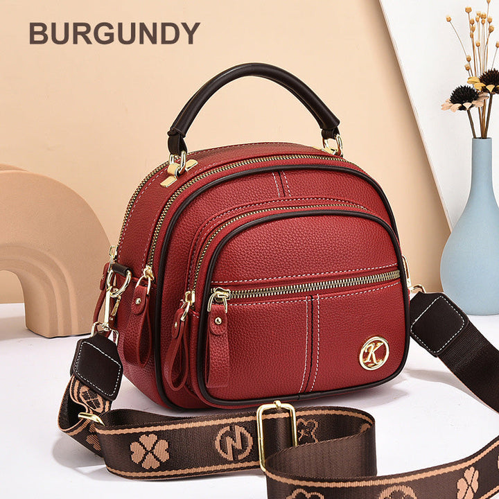 Front view of a burgundy leather crossbody bag with white stitching, a top handle, and a patterned shoulder strap