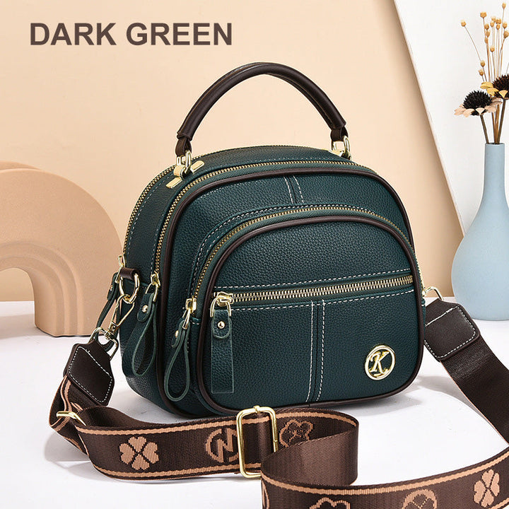 Front view of a dark green leather crossbody bag with white stitching and a patterned shoulder strap
