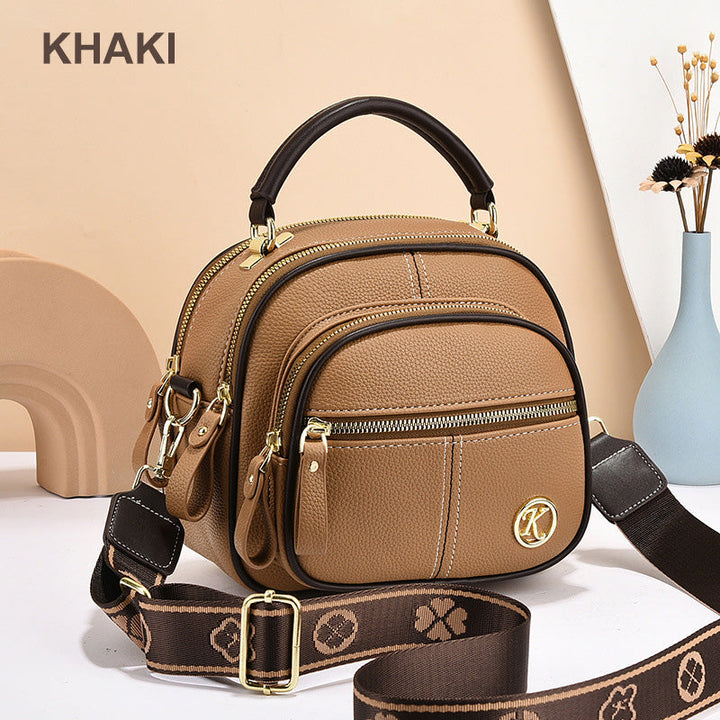 Side view of a khaki leather crossbody bag with a dark top handle and a patterned shoulder strap