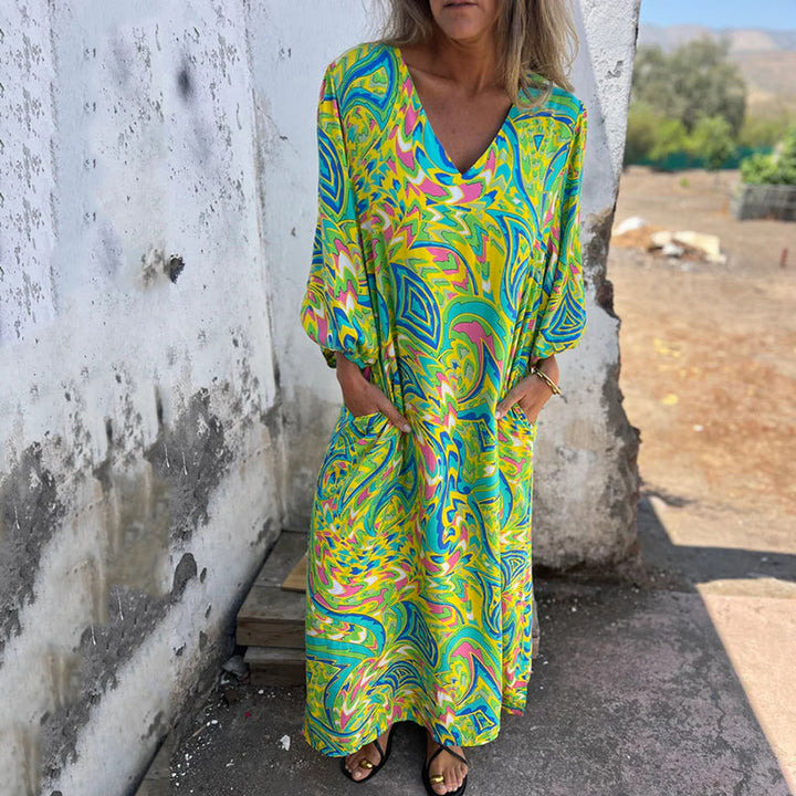 Front view, model wearing a colourful abstract print V-neck maxi dress with long sleeves and hands in pockets