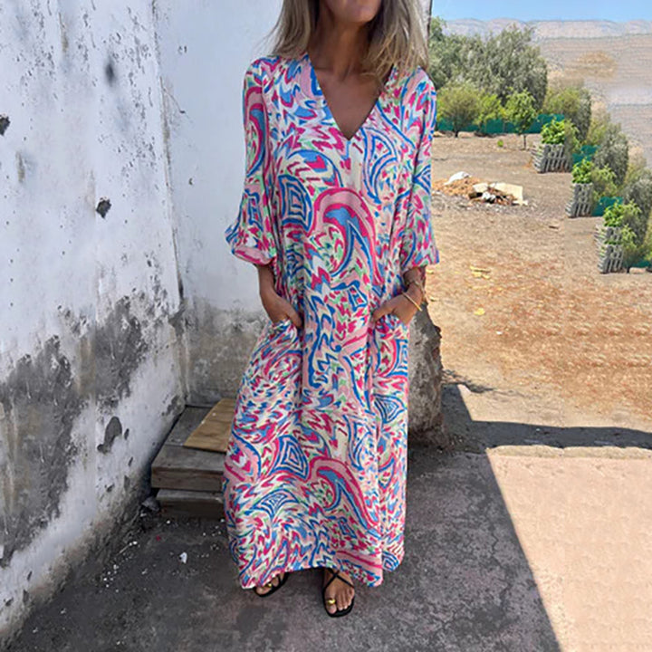 Front view, model wearing a V-neck maxi dress with a colourful abstract print and hands in pockets