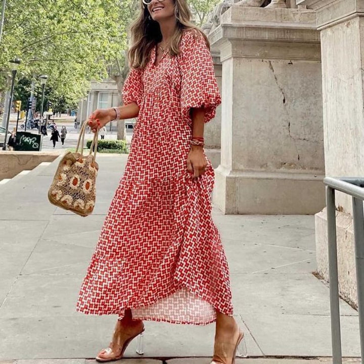Side view of a woman wearing a red and white geometric print boho puff sleeve maxi dress with a crochet bag