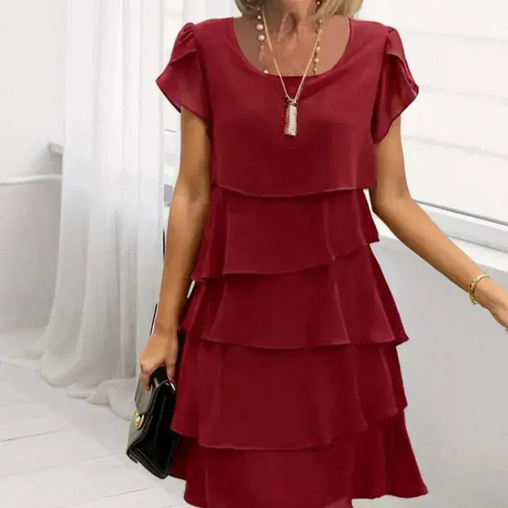 Worn by model, a woman in a red casual ruffled wavy cut dress with layered design, holding a black handbag