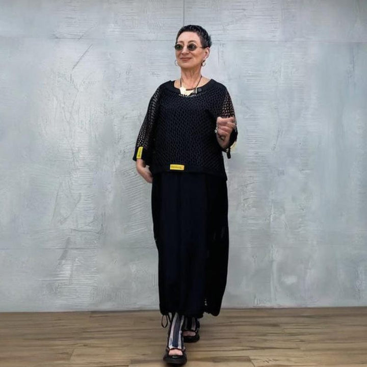 Front view, model wearing a black sleeveless wrap dress with a black mesh top and striped leggings