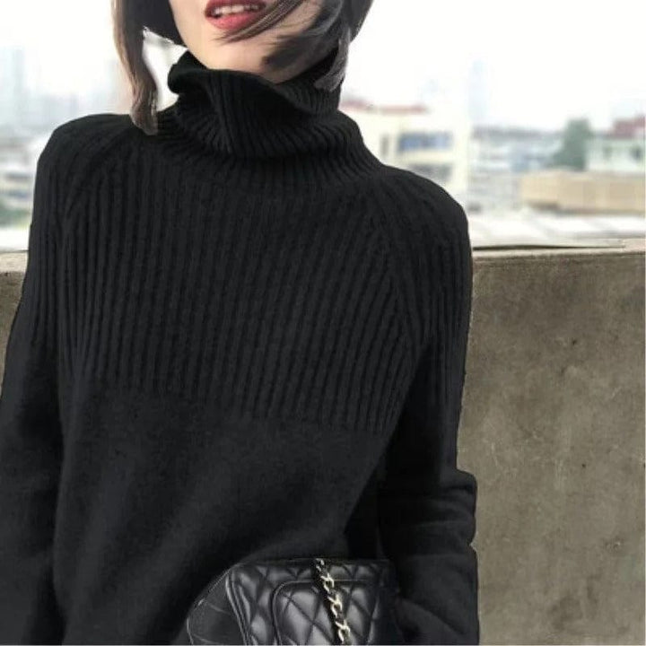 Close up view of a model wearing a soft black ribbed turtleneck jumper with a quilted shoulder bag