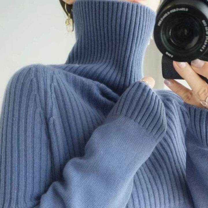 Close up view of a model wearing a soft blue ribbed turtleneck jumper and holding a camera