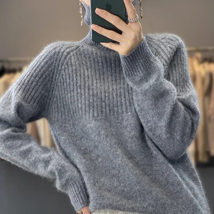 Close up view of a model wearing a soft grey ribbed turtleneck jumper and holding a phone