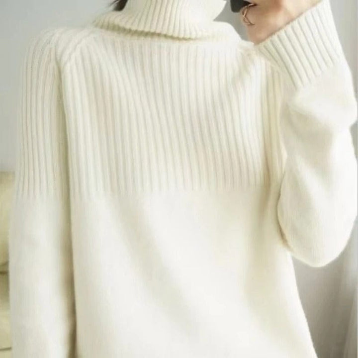 Close up view of a model wearing a soft cream ribbed turtleneck jumper with a gold ring