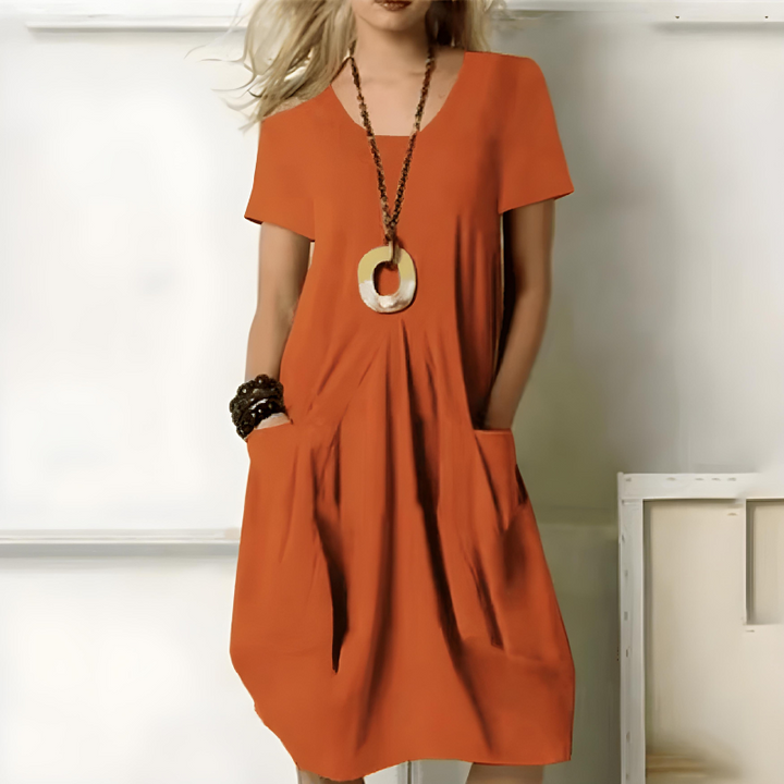 Front view of a model wearing a comfortable rust orange double pocket knee length dress with hands in pockets