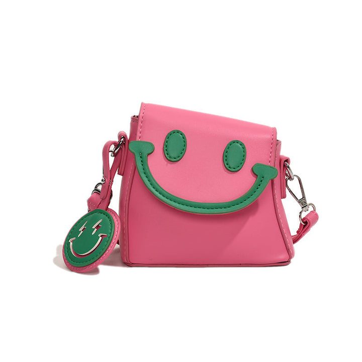 Front view of a pink Bright Smile crossbody bag with green smiley face and keyring against a white background