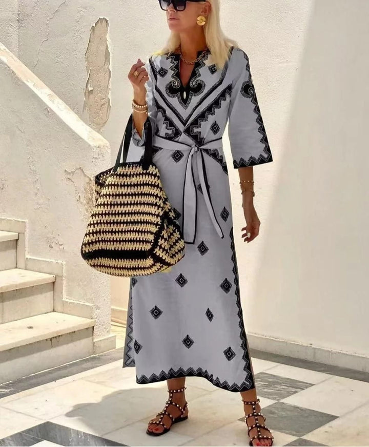 Three quarter view of a model wearing a printed waist tie midi dress with a woven bag and black sandals