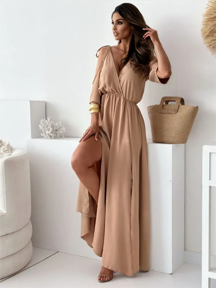 Side view of a model wearing a beige elegant maxi dress with cold shoulder sleeves and a high split