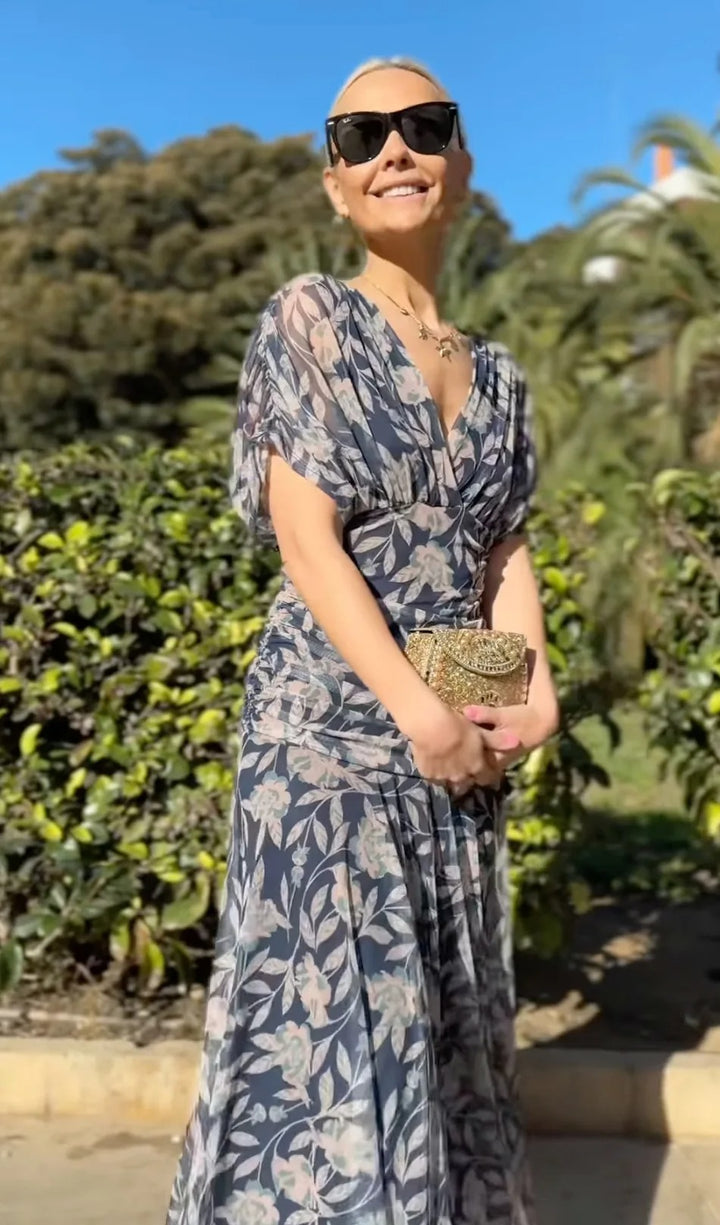 Front view, worn by model, of the Christi Off-Shoulder V-Neck Printed Dress with a gold necklace and clutch, alternate angle