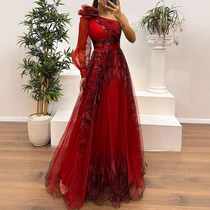 Side view of a model wearing a red single sleeve tulle evening dress with a floral shoulder detail and full skirt