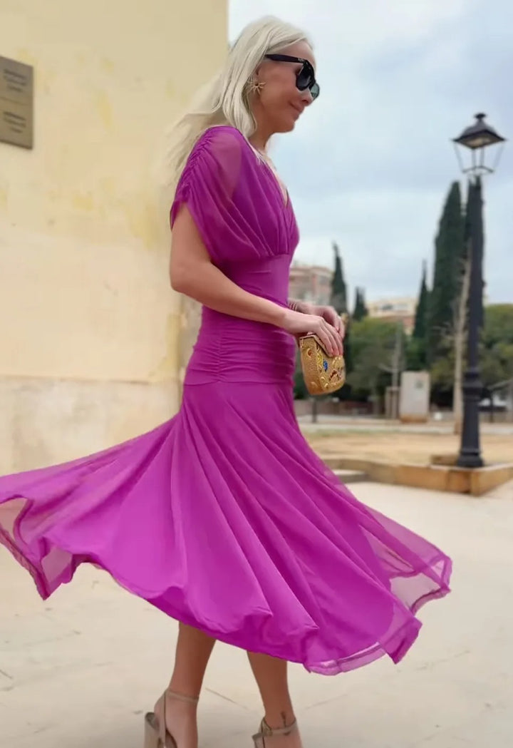 Side view, worn by model, of the Christi Off-Shoulder V-Neck Printed Dress with a gold clutch and heels