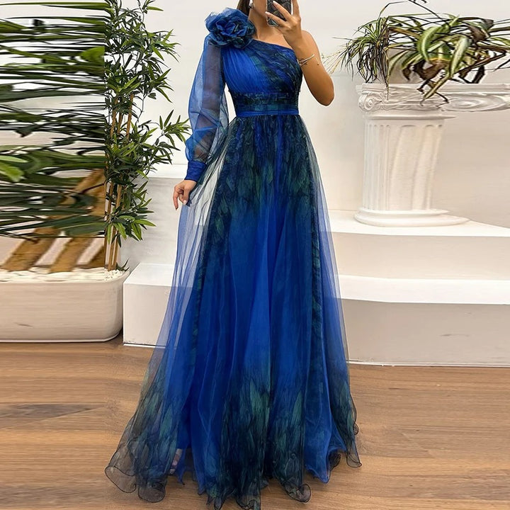 Front view of a model wearing a blue single sleeve tulle evening dress with a floral shoulder detail and full skirt