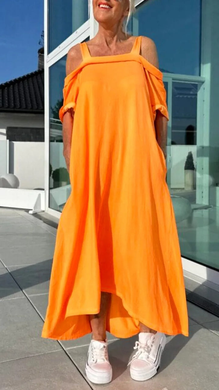 Front view, model wearing an orange Brianna maxi dress with open shoulders and white platform sneakers