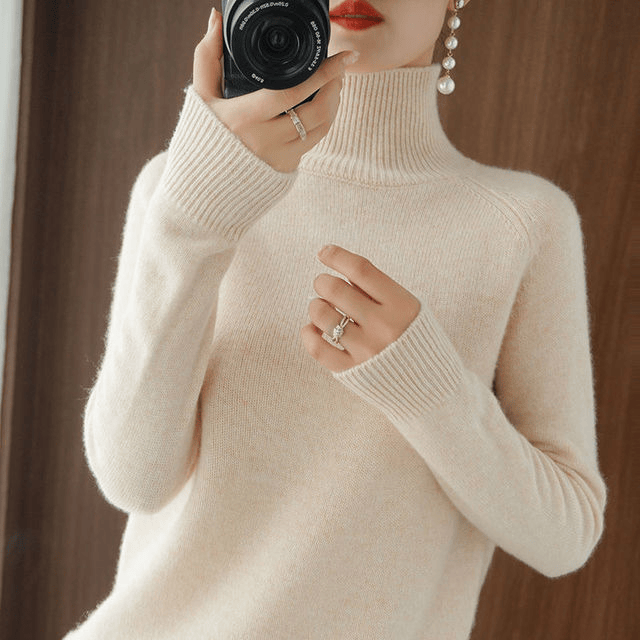 Close up of a model wearing the cream turtleneck jumper with long pearl earrings and a camera
