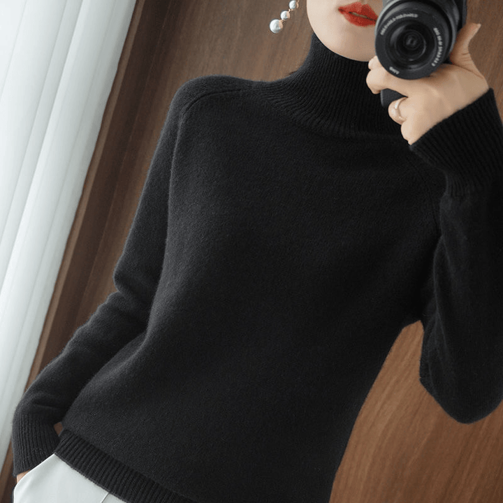 Close up of a model wearing the black turtleneck jumper with pearl earrings and a camera