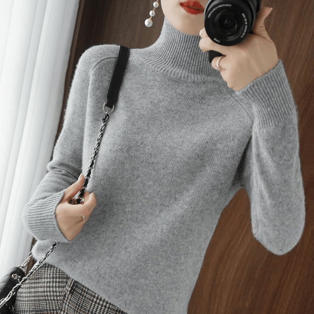 Side view of a model wearing the grey turtleneck jumper with a crossbody bag and camera