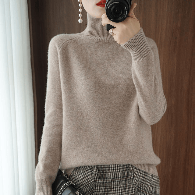 Three quarter view of a model wearing the cream turtleneck jumper with a plaid skirt and a camera
