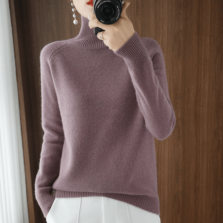 Front view of a model wearing the pink turtleneck jumper with white pants and pearl earrings