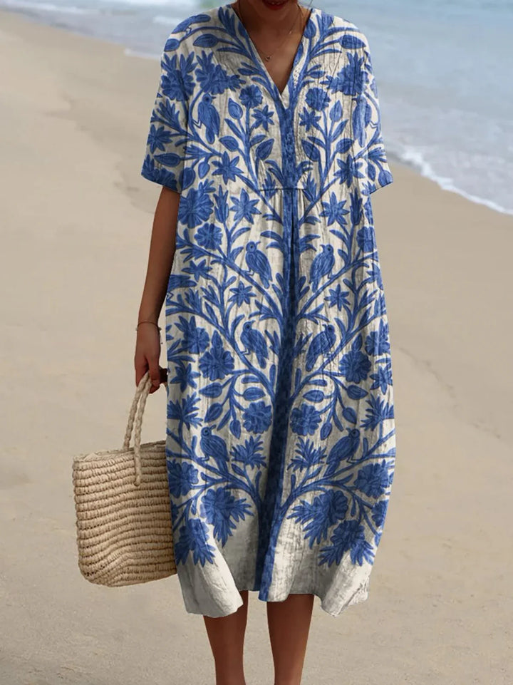 Front view of a model wearing the Claribel embroidered boho blue dress with a woven bag on a beach