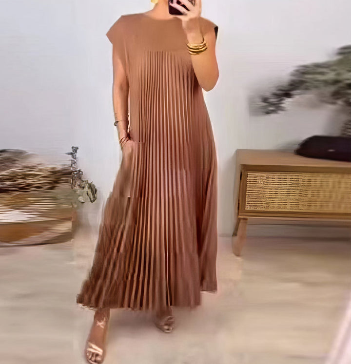 Sleeveless pleated dress, front view worn by model, hand in pocket, holding phone, gold cuffs and sandals