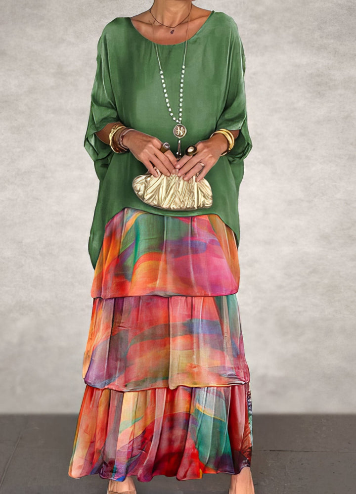 Front view of a woman wearing an Artistic Flow Dress with a tiered skirt, gold clutch and long necklace