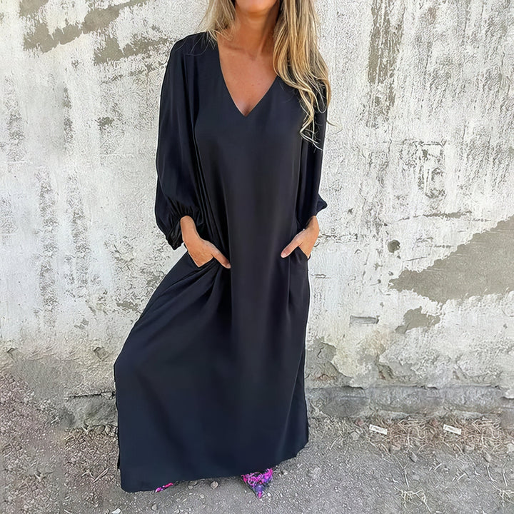 Front view of a woman wearing a black bohemian maxi dress with pockets, hands in pockets