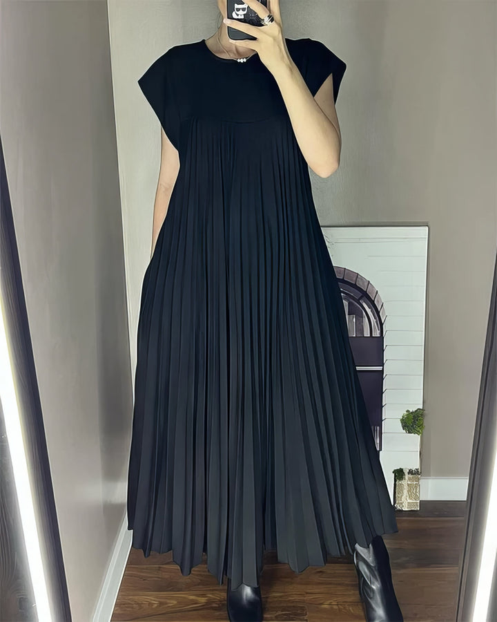Sleeveless pleated dress, front view worn by model, holding phone, black boots and pearl necklace