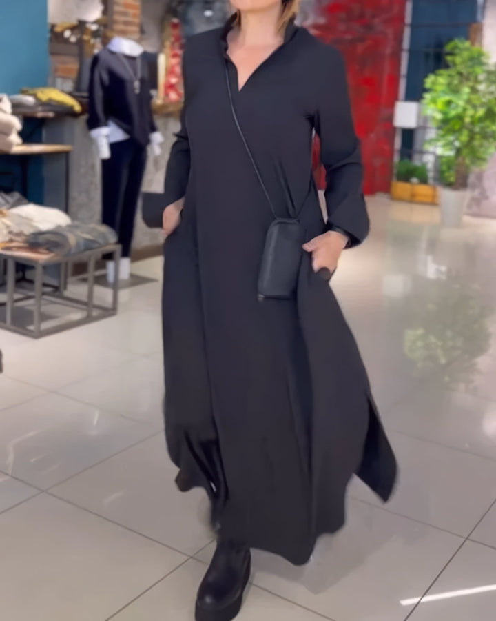Front view, model wearing a black stretch maxi dress with a V-neck and long sleeves, hands in pockets