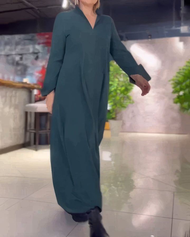 Side view, model wearing a dark green stretch maxi dress with a V-neck and long sleeves, walking indoors