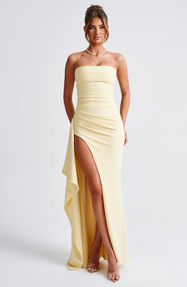 Front view of a model wearing a strapless elegant high split maxi dress in pale yellow with a pearl necklace