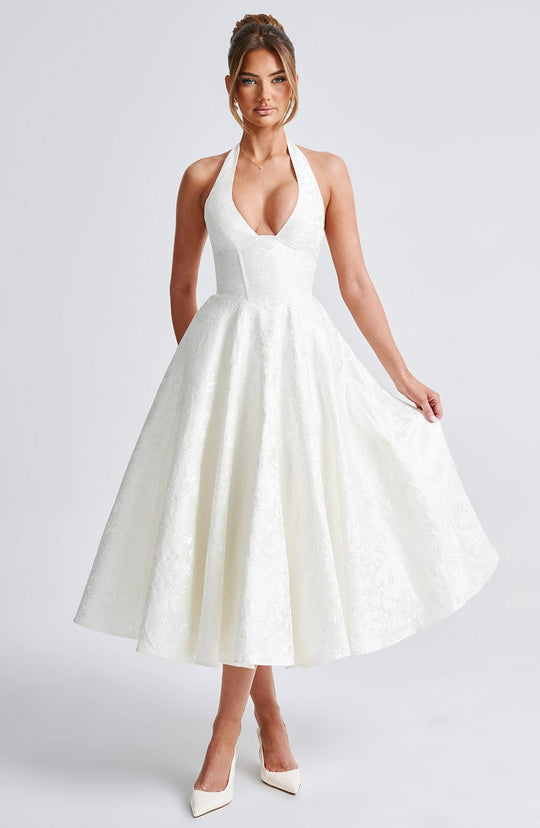 Front view, model wearing a white jacquard halter neck midi dress with a full skirt and white heels