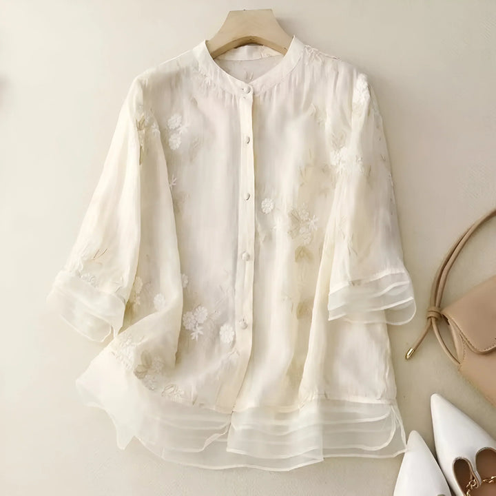 Front view of a white lightweight cotton blouse with delicate floral embroidery and layered ruffle sleeves