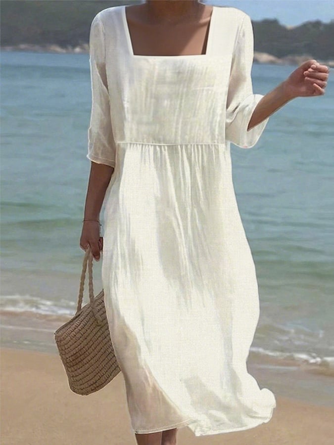 Front view of a model wearing a white cotton linen casual dress with a square neckline on a beach