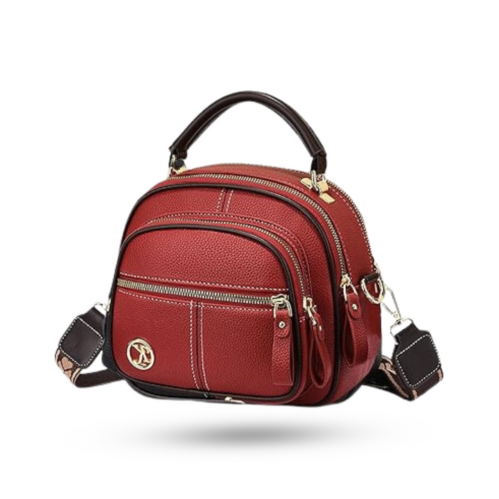 Front view of a red leather crossbody bag with multiple zips, a top handle, and a patterned shoulder strap
