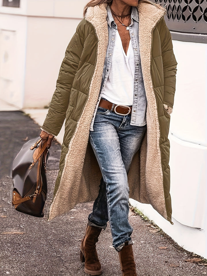 Front view, model wearing a long khaki reversible quilted hooded coat with cream sherpa lining over a white top and jeans