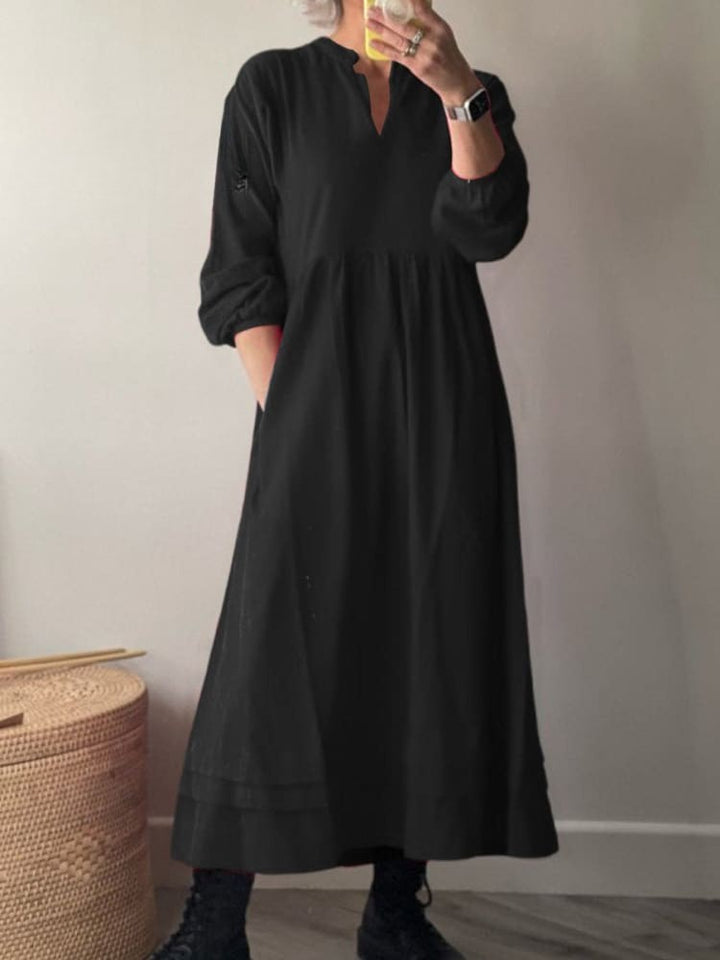 Front view, model wearing a black cotton dress with pockets, long sleeves, and a v-neckline