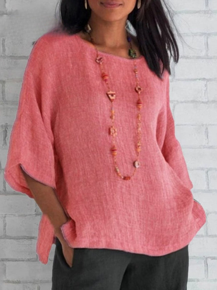 Front view of a model wearing a coral pink crewneck cotton linen shirt top with a long beaded necklace
