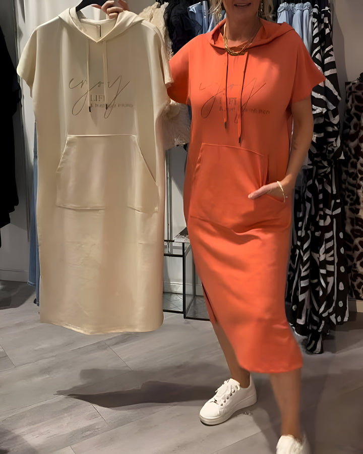 Front view of a model wearing an orange hooded sweatshirt dress with pockets, another cream dress held next to her