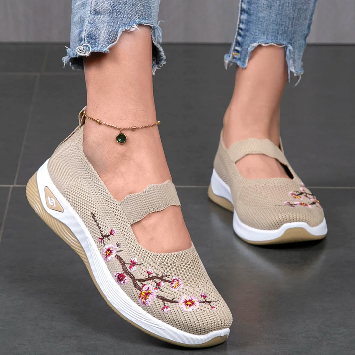 Close up of model wearing beige slip-on sneakers with pink floral embroidery and an ankle bracelet