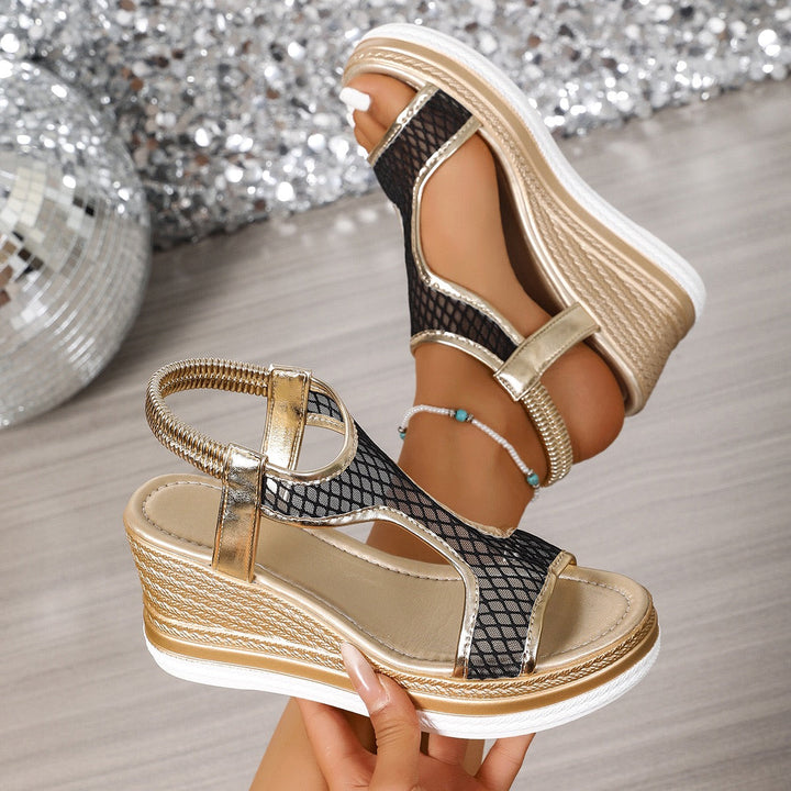 Worn by model, a pair of elegant gold and black arch-support wedge sandals with mesh detail and ankle strap