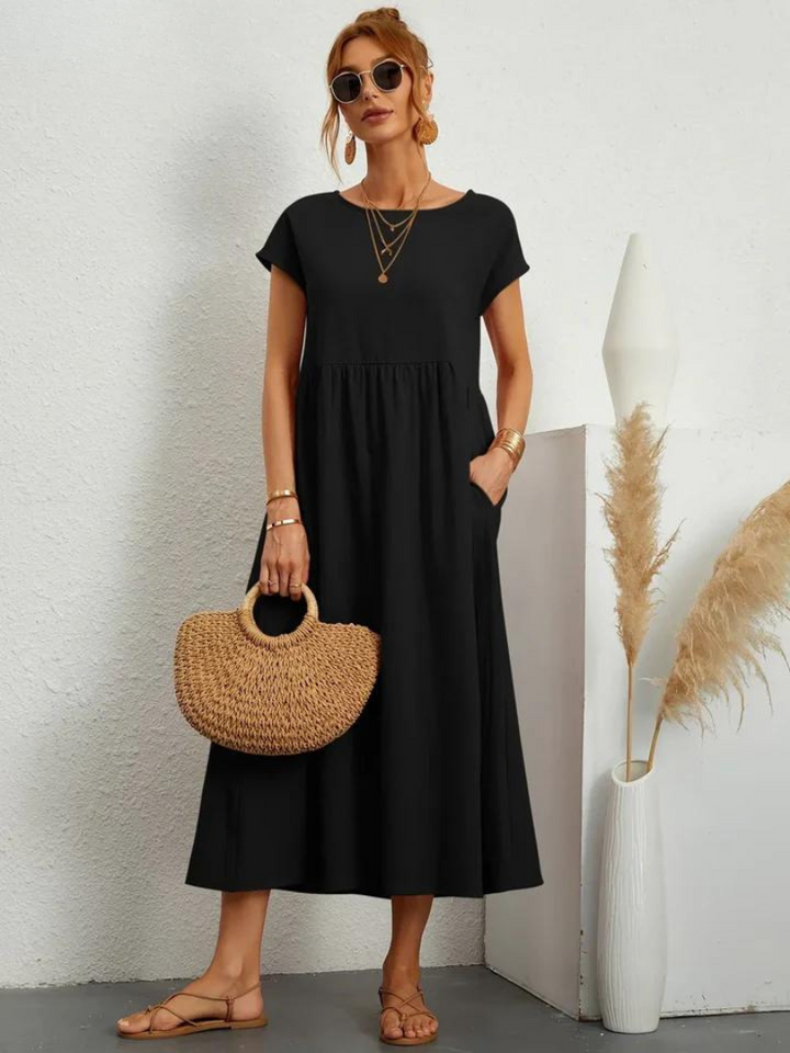 Front view, model wearing a black loose summer dress with short sleeves, sunglasses and a straw handbag