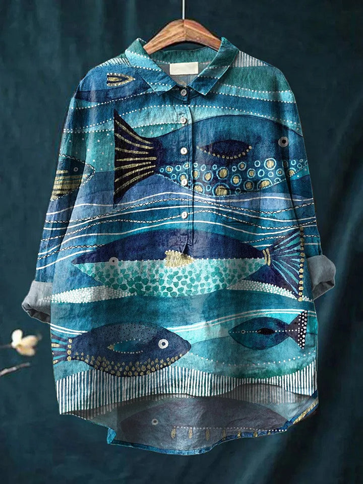 Front view of an ocean-inspired art shirt with blue fish and wave patterns on a wooden hanger